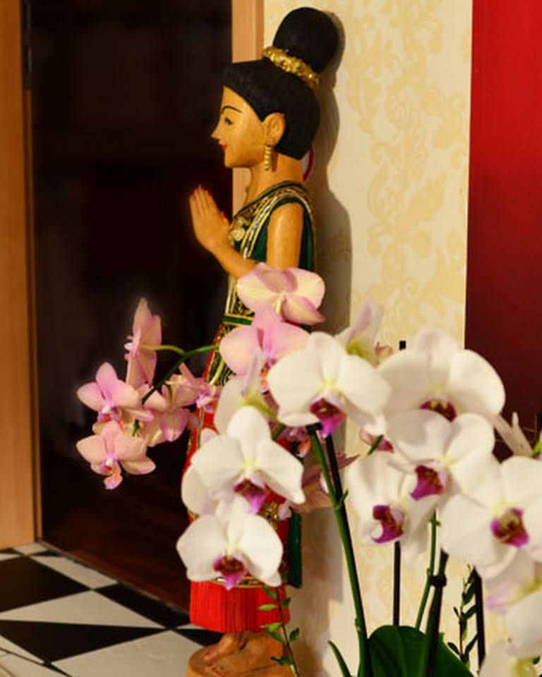 Thailändische Holzfigur und weiße Orchideen am Eingang des Studios